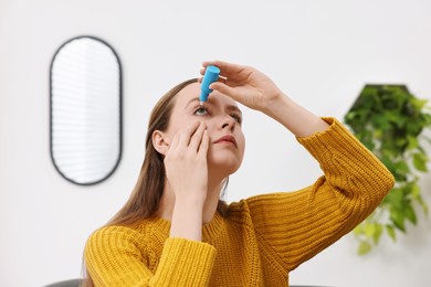 Photo of Young woman applying medical eye drops indoors