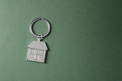 Photo of Metallic keychain in shape of house on dark green background, top view. Space for text