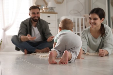 Photo of Happy parents watching their baby crawl on floor at home