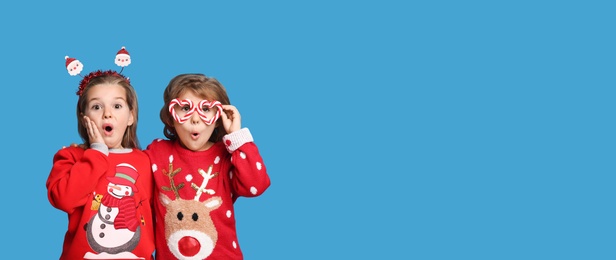 Kids in Christmas sweaters and festive accessories on blue background, space for text