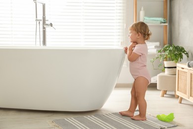 Photo of Cute little girl near tub in bathroom