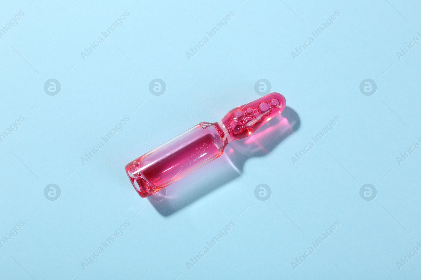 Photo of Glass ampoule with liquid on light blue background, top view