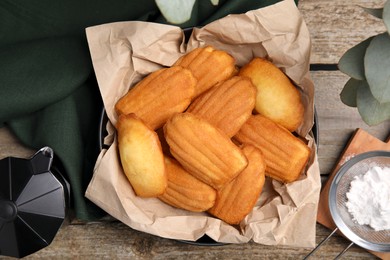 Photo of Delicious madeleine cakes, powdered sugar and coffee maker on wooden table, flat lay