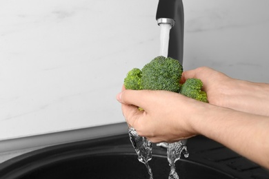 Photo of Woman washing fresh green broccoli in kitchen sink, closeup view. Space for text