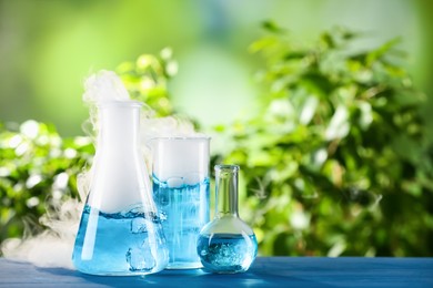 Photo of Laboratory glassware with colorful liquids on blue wooden table outdoors, space for text. Chemical reaction