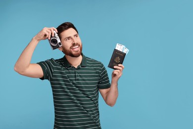 Smiling man with passport, camera and tickets on light blue background. Space for text