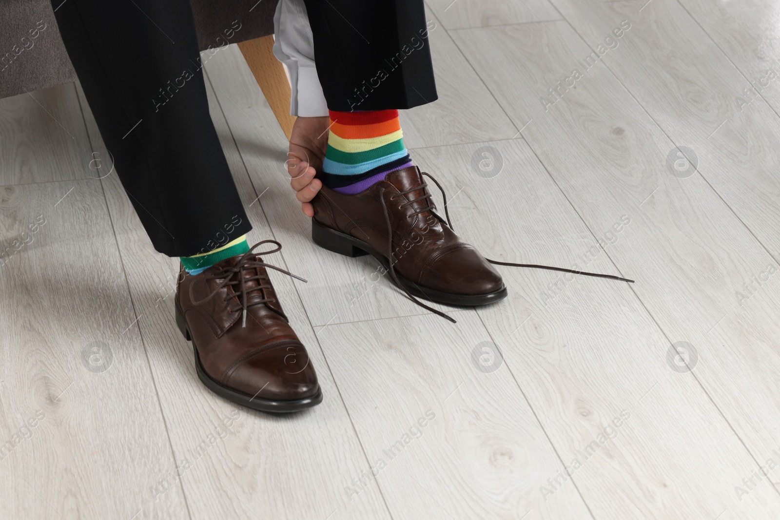 Photo of Man with colorful socks putting on stylish shoes indoors, closeup