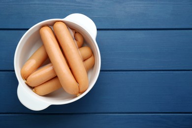Photo of Bowl of delicious sausages on blue wooden table, top view. Space for text
