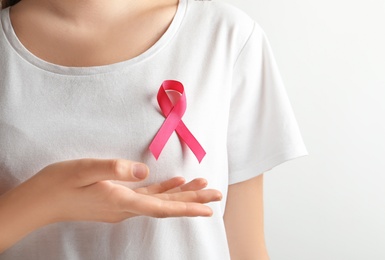 Photo of Woman with pink ribbon on t-shirt against light background. Cancer awareness