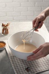 Photo of Woman whipping ingredients with whisk at light grey table, closeup. Cooking delicious eggnog