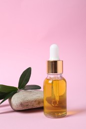 Bottle with cosmetic oil, green leaves and stone on pink background. Space for text