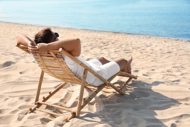 Photo of Young man relaxing in deck chair on sandy beach