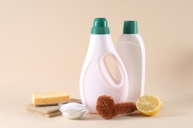 Photo of Bottles of cleaning product, sponges, brush and baking soda on beige background