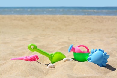 Photo of Bright plastic rake and shovel on sand near sea. Beach toys. Space for text