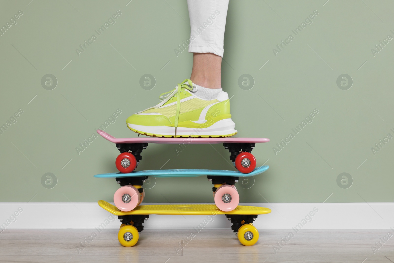 Photo of Woman in new stylish sneaker standing on skateboards near light green wall, closeup