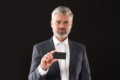 Photo of Handsome businessman holding blank business card on black background