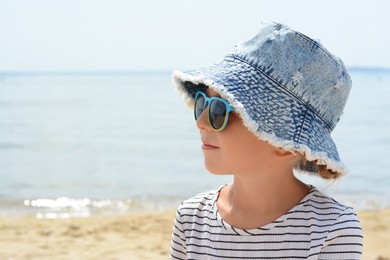 Photo of Little girl wearing sunglasses and hat at beach on sunny day. Space for text
