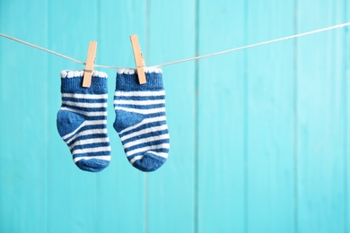 Baby socks on laundry line against color wooden background, space for text. Child accessories
