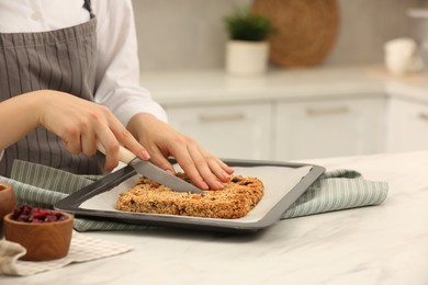 Photo of Woman cutting granola bars at table in kitchen, closeup