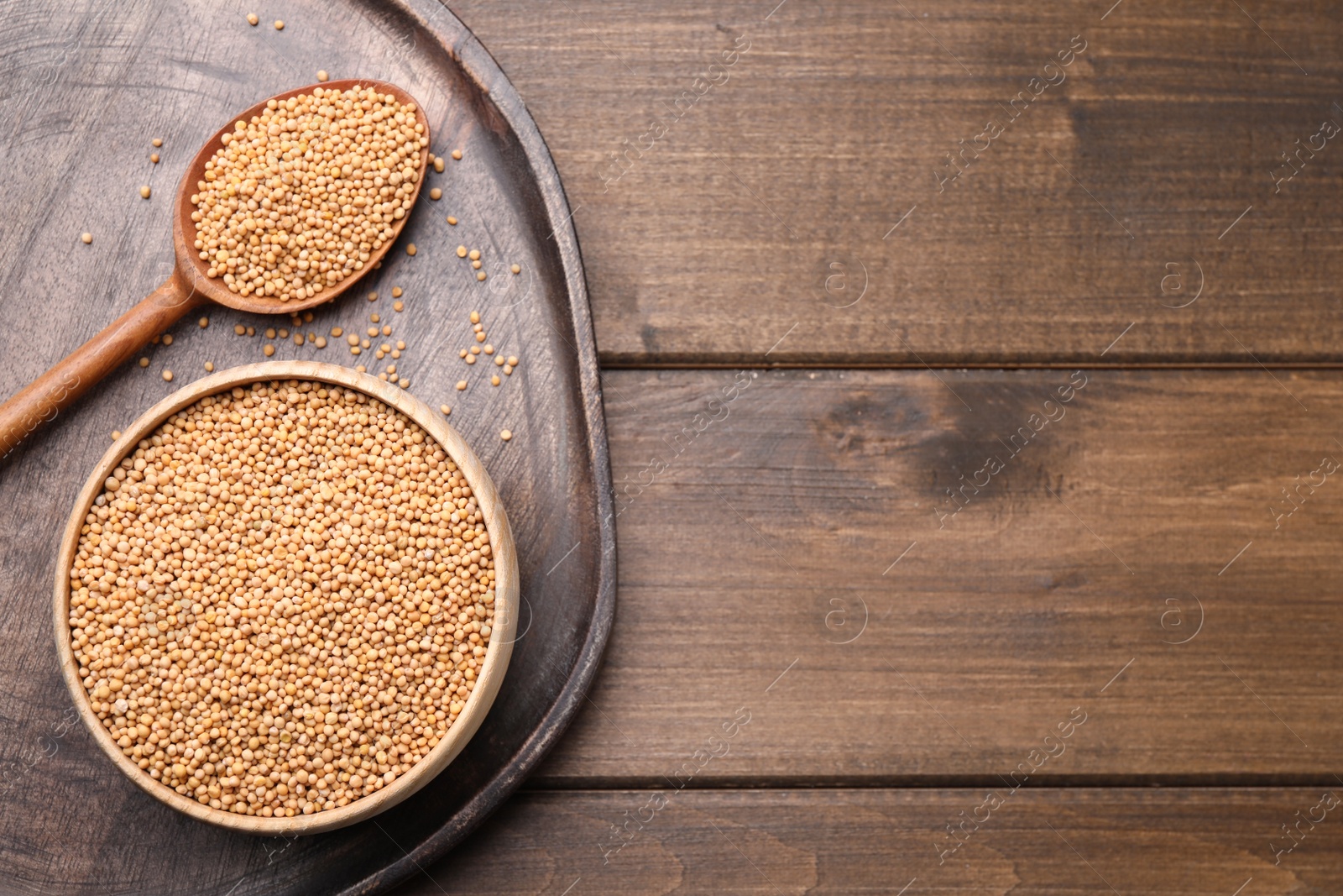 Photo of Mustard seeds with bowl and spoon on wooden table, flat lay. Space for text