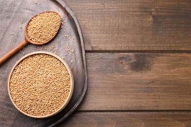 Photo of Mustard seeds with bowl and spoon on wooden table, flat lay. Space for text