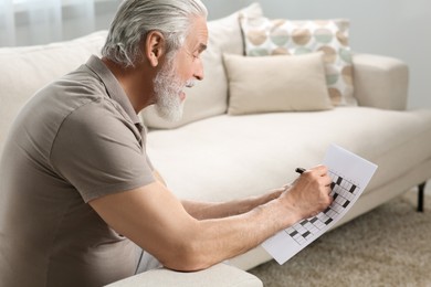 Senior man solving crossword on sofa at home
