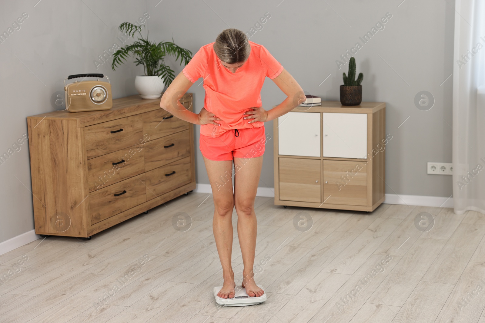 Photo of Woman in sportswear standing on floor scales at home