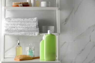 Photo of Stack of towels, brushes, shampoo and other toiletries on shelves near white marble wall