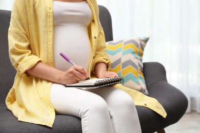Photo of Pregnant woman writing baby names list on sofa, closeup