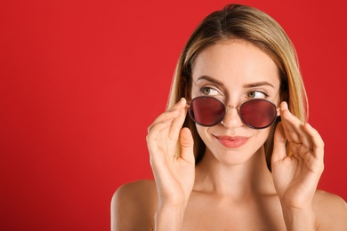 Photo of Beautiful woman in stylish sunglasses on red background. Space for text