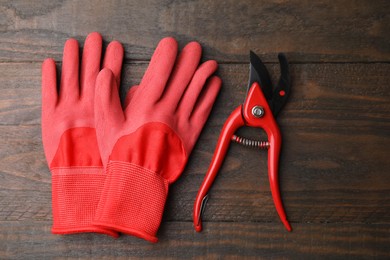 Photo of Pair of red gardening gloves and secateurs on wooden table, top view