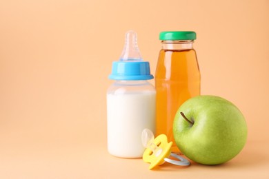 Photo of Juice, milk, apple and pacifier on pale orange background, space for text