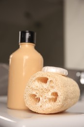 Photo of Natural loofah sponge and shower gel bottle on washbasin in bathroom, closeup