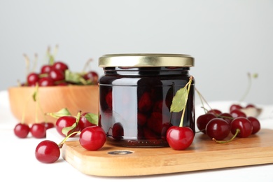 Photo of Jar of pickled cherries and fresh fruits on white table