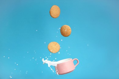 Photo of Delicious cookies and cup of milk falling on light blue background
