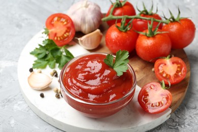 Photo of Delicious ketchup in bowl, parsley, garlic and tomatoes on grey textured table, closeup