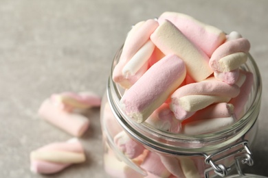 Photo of Glass jar with tasty marshmallows on light grey table, closeup. Space for text