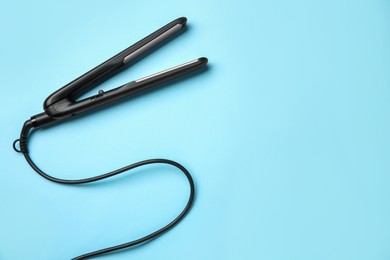 Photo of Modern flat hair iron on light blue background, top view. Space for text