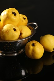 Photo of Tasty ripe quinces and metal colander on black mirror surface, closeup