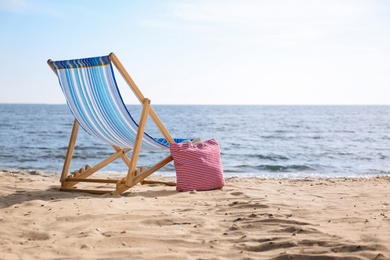 Photo of Lounger and bag on sand near sea, space for text. Beach objects