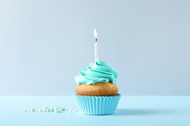 Photo of Delicious birthday cupcake with candle on light background