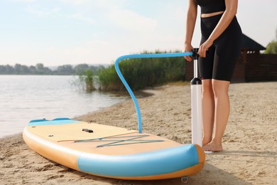 Photo of Woman pumping up SUP board on river shore, closeup