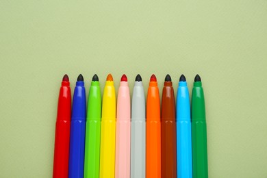 Photo of Different colorful markers on light green background, flat lay. Space for text