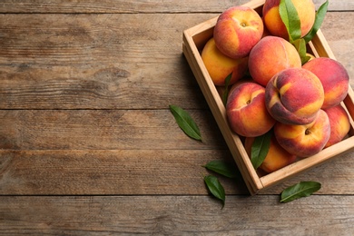 Photo of Fresh sweet peaches in wooden crate on table, top view. Space for text