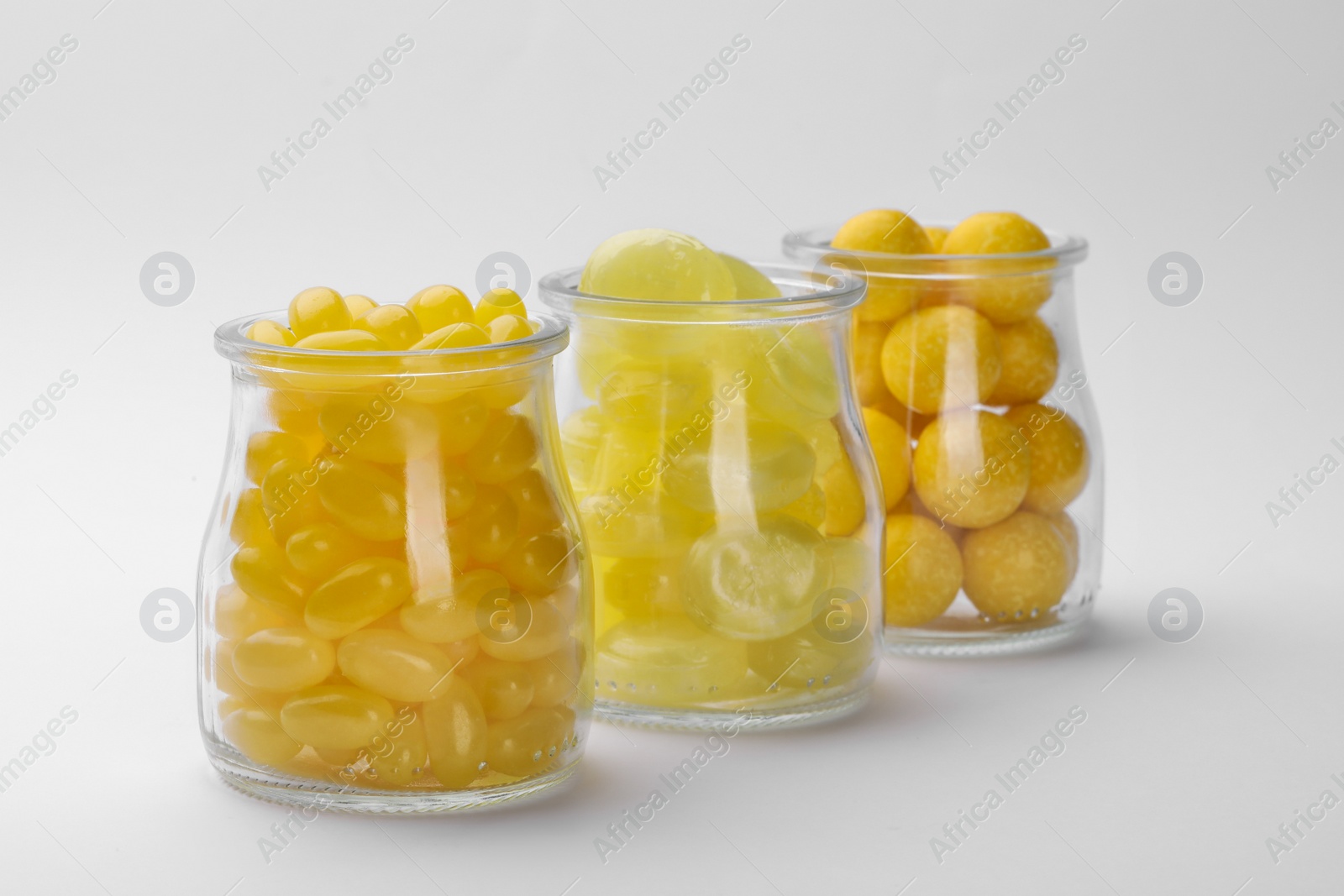 Photo of Different tasty lemon drops in jars isolated on white