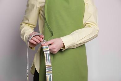 Photo of Woman putting on green apron against white wall, closeup