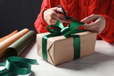 Photo of Christmas present. Woman decorating gift box at white wooden table, closeup