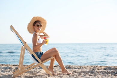 Photo of Young woman with cocktail in beach chair at seacoast. Space for text