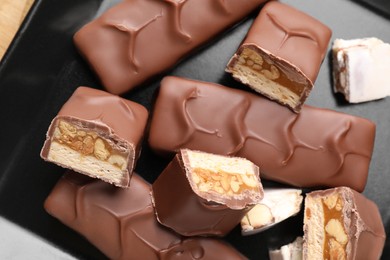 Photo of Tasty chocolate bars with nougat and nuts on black plate, top view