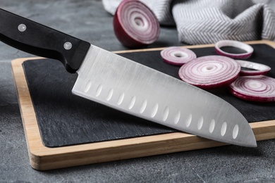 Photo of Board with sharp knife and cut onion on grey background